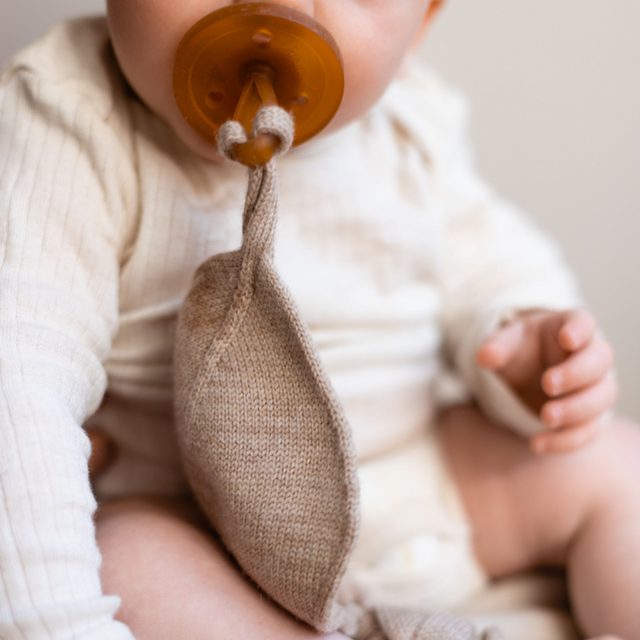 Baby in white long-sleeve bodysuit with natural dummy with sand beige Merino wool knitted comforter dummy chainattached