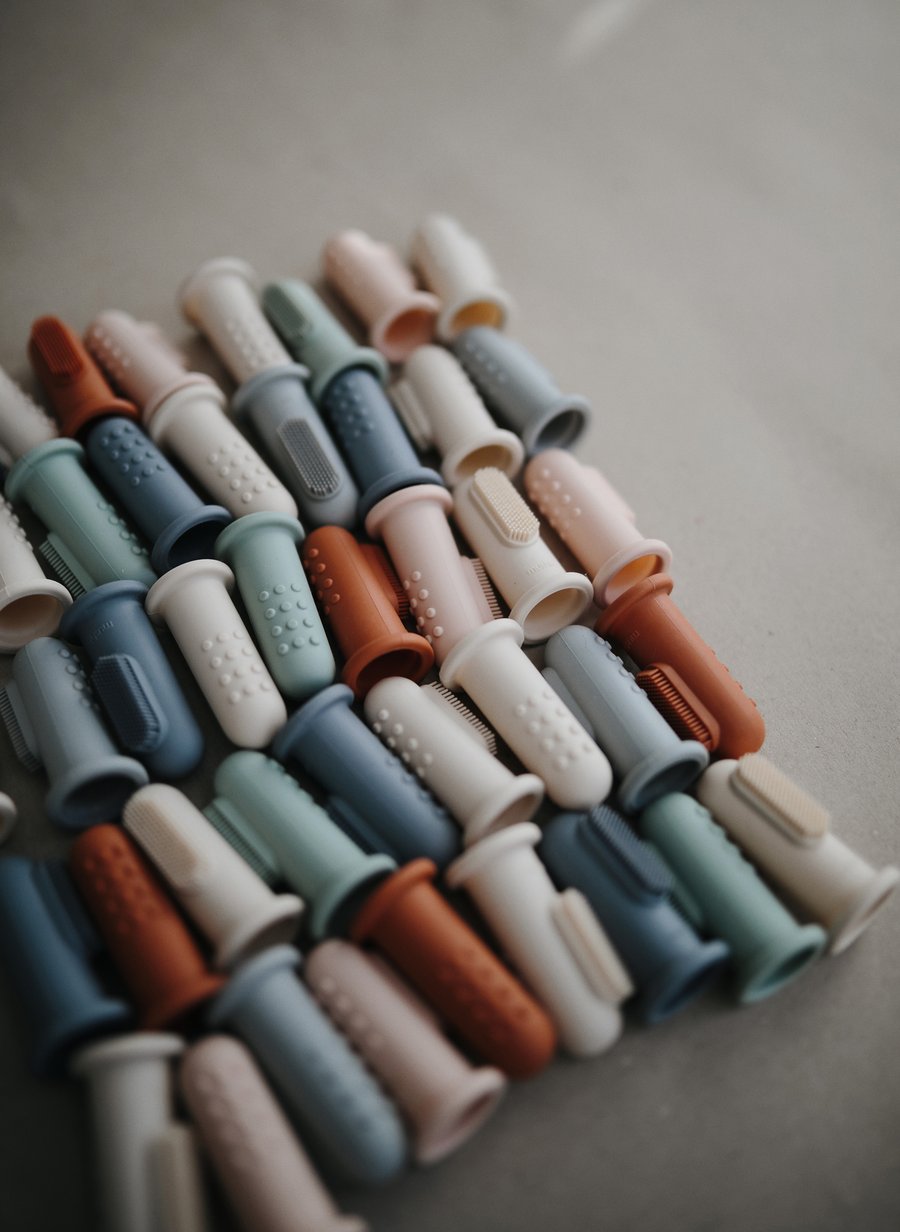 BLue, green, pink and beige finger toothbrushes lined up 