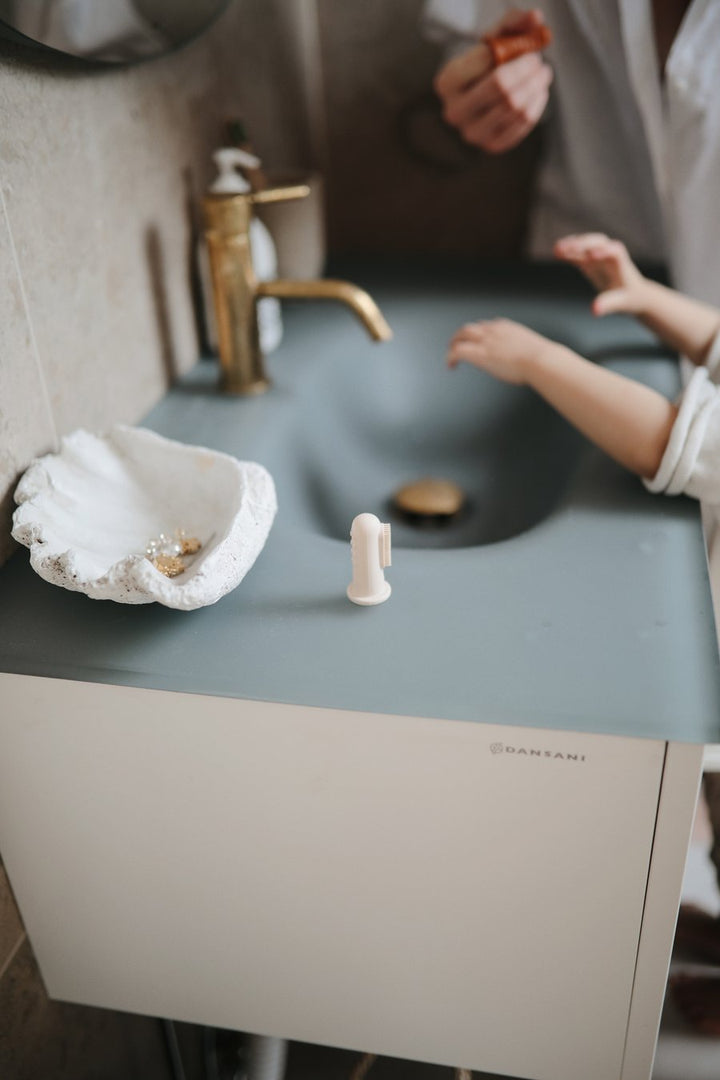 Bathroom sink with beige baby finger toothbrush next to it
