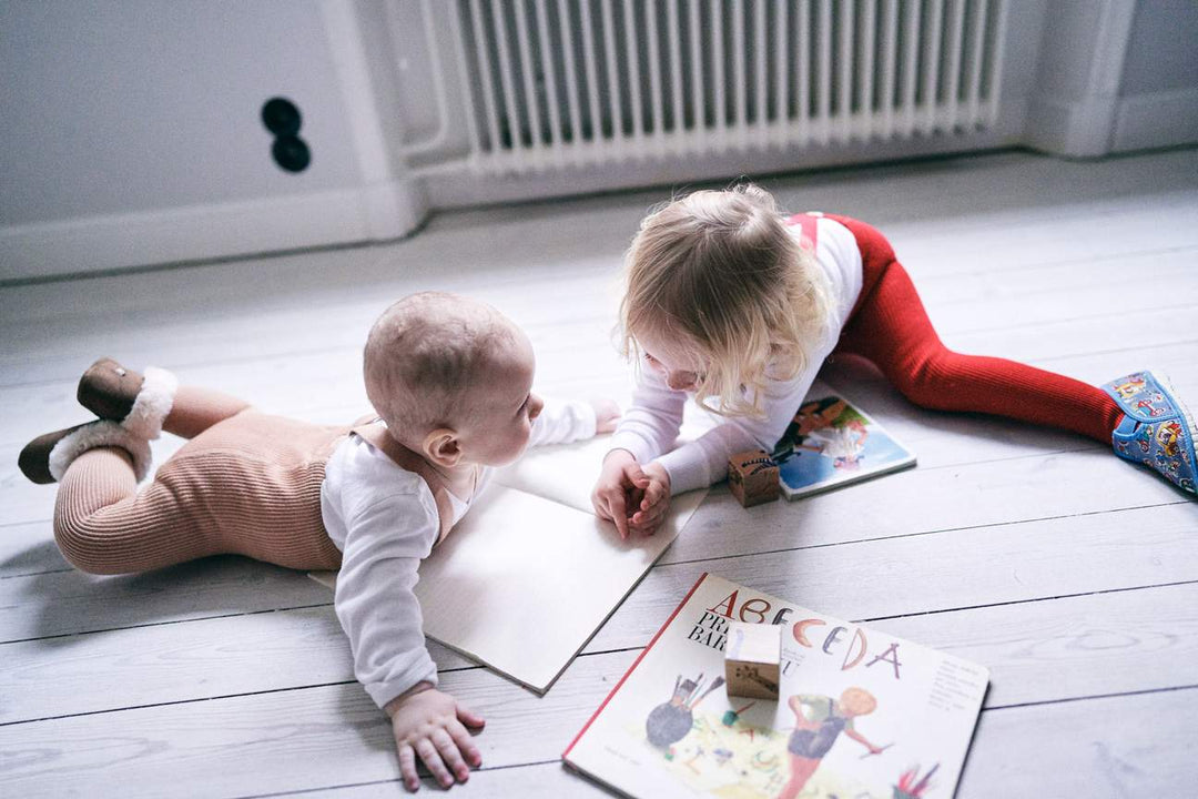 Baby and toddler reading books on floor Baby wearing Silly Silas light brown rib tights with braces