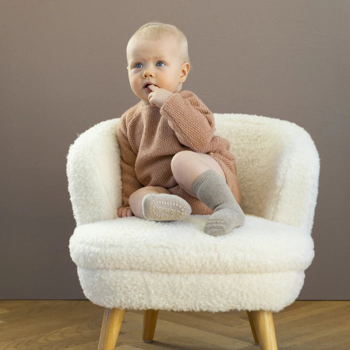 GoBabyGo cotton Terry non-slip socks wit rubber pads in sand beige worn by baby sit-in on white teddy fabric armchair