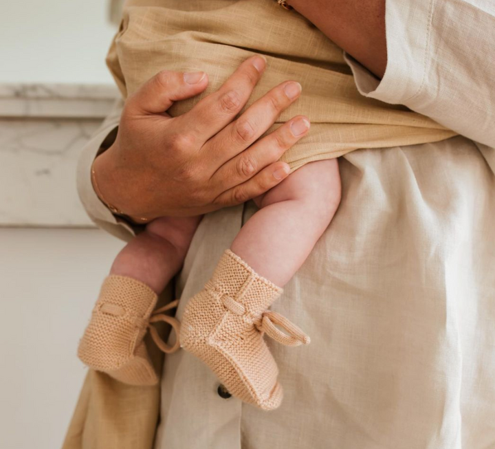 Baby wearing paricot pink blush knitted Merino wool booties held by parent