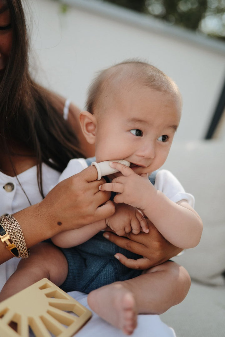 Mother brush baby's teeth with beige finger toothbrush