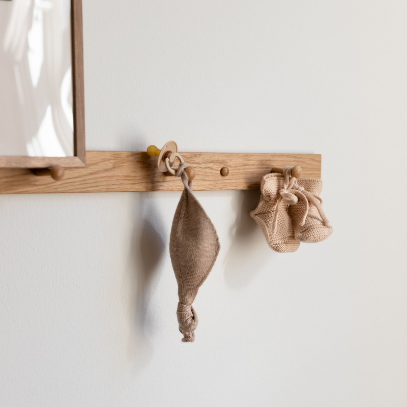 Wooden wall attached coat rack with Merino wool beige knitted comforter on dummy chain and apricot blush knitted baby booties