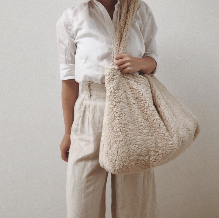 Women in wjite blouse and beige linen pants carrying shoulder large shopper bag with handles white off-white beige ecru teddy boucle fabric