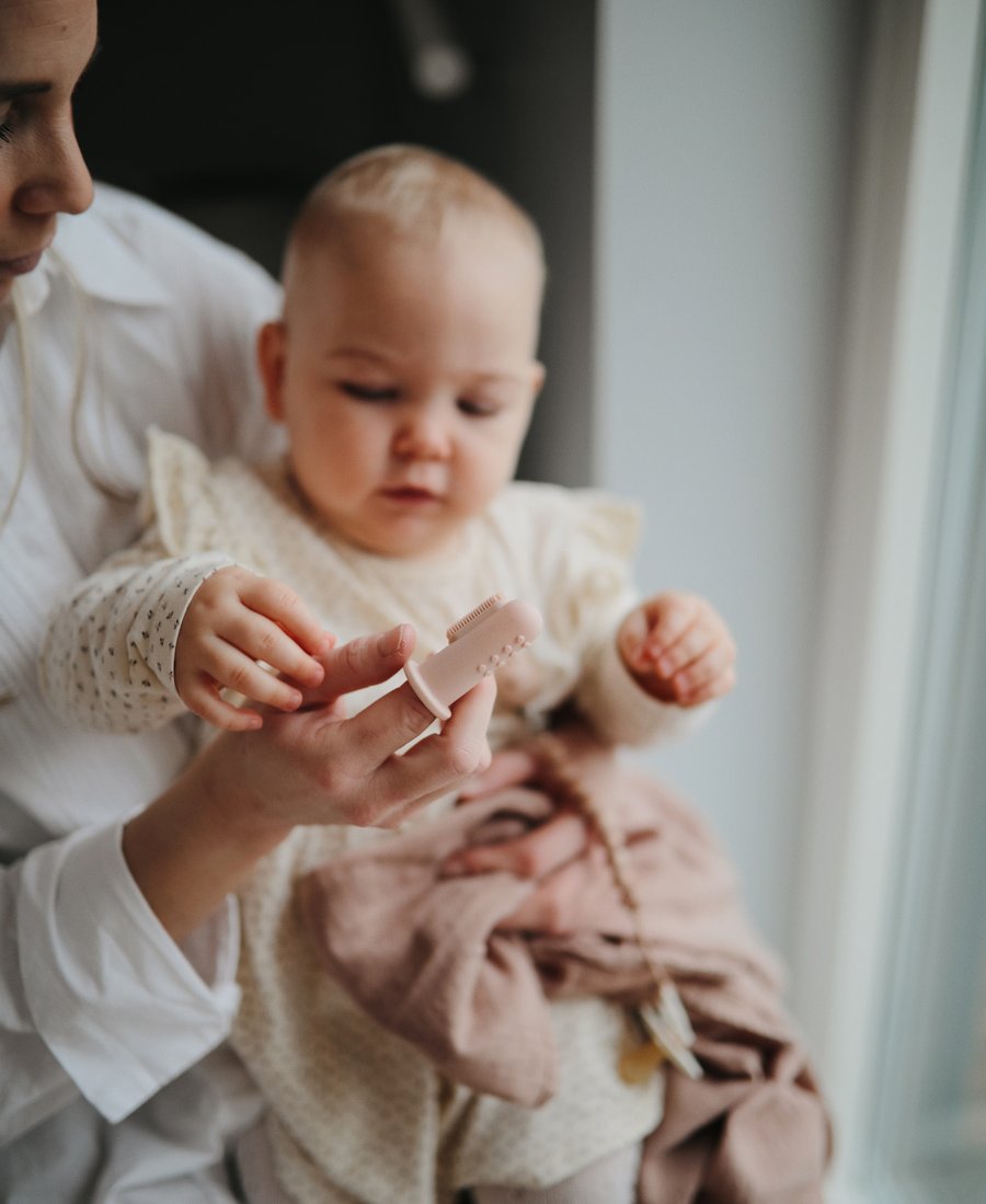 Mother holding baby girl and pink blush finger toothbrush 