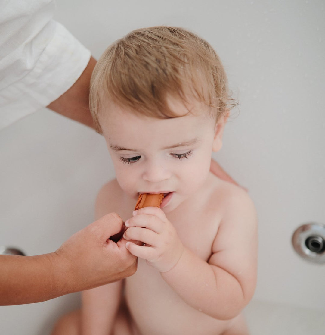 Baby boy brushing teeth with brown finger toothbrush 